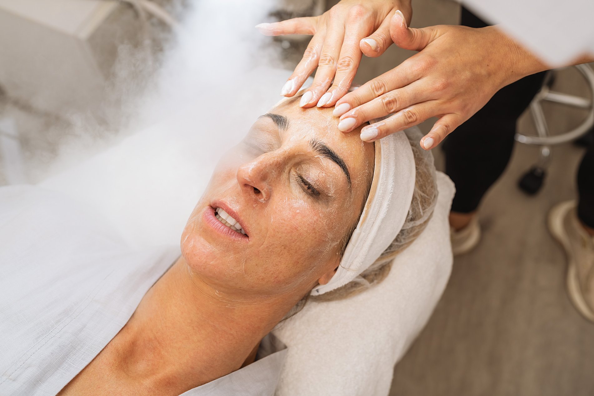 Beauty treatment of a woman with ozone facial steamer and cream