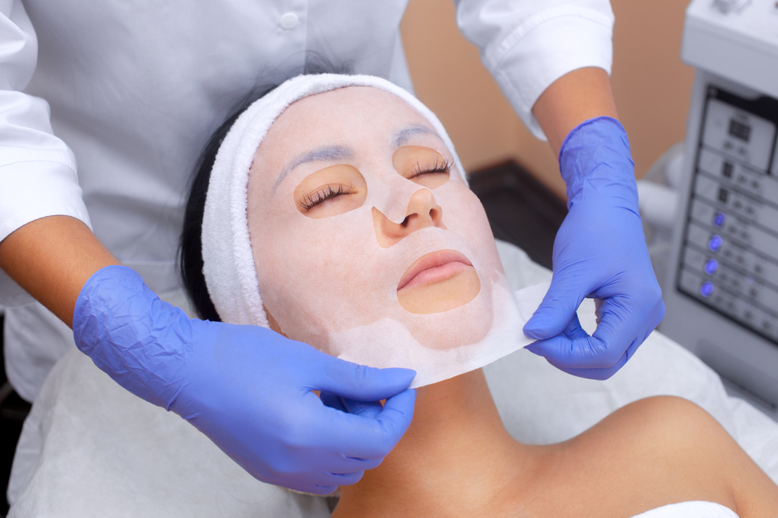 The cosmetologist for procedure of cleansing and moisturizing the skin, applying a sheet mask to the face